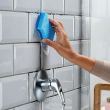 Hand holding a blue scrub sponge against tiled backsplash near a sink