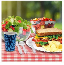 Scalloped white paper plate on picnic table with sandwich and salad