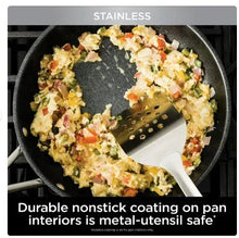 Skillet with black nonstick interior holding cooked vegetables, with white spatula