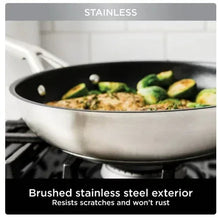 Brushed stainless steel frying pan with black interior on stovetop, cooking vegetables
