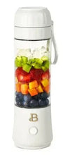 White portable to-go blender with clear jar and mixed fruit inside, handled lid