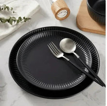 Black stoneware dinner plate with ribbed rim, spoon and fork set on top