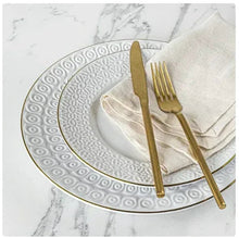 Stoneware dinner plate with embossed swirl rim, gold trim, and tableware on napkin