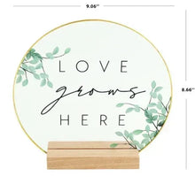 Translucent oval tabletop plaque with gold cursive "Love grows here" and wood stand