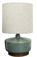 Ceramic table lamp with dark green base and light fabric drum shade.