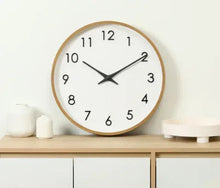 Round analog wall clock with mid-tone wood frame, white dial, black hands, Arabic numerals