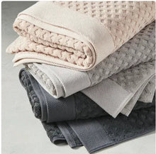 Stack of bath towels in beige and gray with textured pattern and rolled folds.