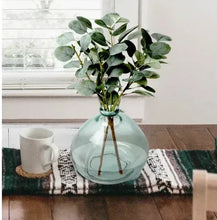 Artificial eucalyptus in teal blown-glass vase with three stems, on tabletop display