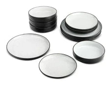 Ceramic dinnerware set: white speckled plates and bowls with black rims, stacked.