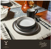 Stacked ceramic plates and bowls on table setting, white speckled with black rims.