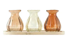 Three translucent glass bud vases on natural wood tray, amber, pale green, orange