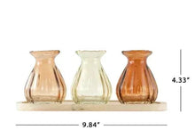Three translucent glass bud vases on natural wood tray in amber, pale green, orange