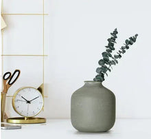 Green metal tabletop vase with eucalyptus sprigs, rounded body and short neck.