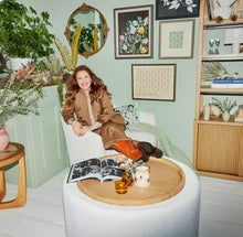 Round gold ornate mirror against wall, shown with seated person