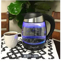 Glass electric tea kettle with stainless base, black handle, blue-lit water inside.