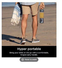 Portable blender with clear cup and denim-blue base, carried with hand.