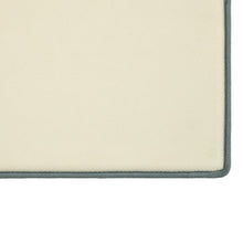 Cream bath mat corner with dark gray border and textured surface