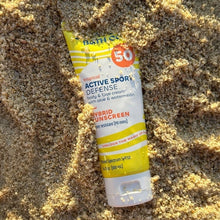 SPF 50 sunscreen lotion tube in yellow and white, outdoors on sand.