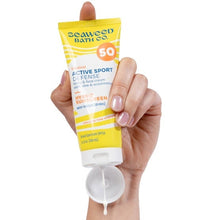 SPF 50 sunscreen lotion tube held in hand, yellow cap and white base.