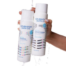 Shampoo and conditioner bottles held in hands, unscented, white with blue wave labels
