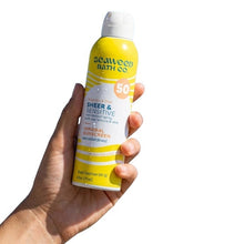 Mineral sunscreen spray bottle, SPF 50, held in hand; yellow with white cap