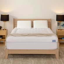 White mattress topper with quilted pillowtop surface and logo label, on bed frame