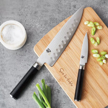 Chef’s knife with black handle and silver patterned blade on wooden cutting board