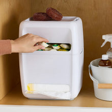 Under-sink trash bag and dish pod organizer with hand placing dish pods