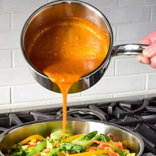 Stainless steel saucepan with long handle, orange sauce being poured into pot