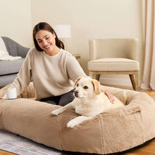 Beige plush dog bed with cushioned sides and front paw-print opening