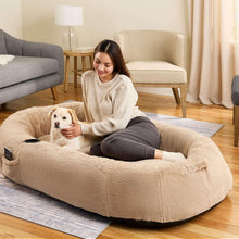 Beige oversized plush dog bed with curled, human-cuddler shape and raised rim