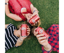 Dr. Pepper soda cans held by people outdoors on grass