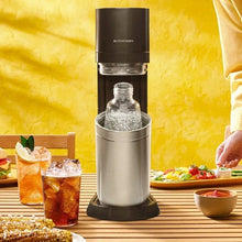 Sparkling water maker dispensing bubbles into glass bottle with stainless carafe