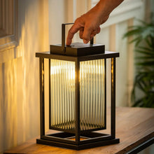 Black solar LED lantern with glass panels, warm light glowing inside.