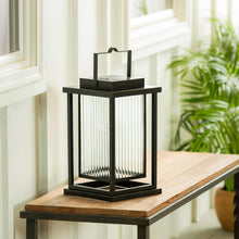 Black solar LED lantern on porch step, clear side panels with bright glow.