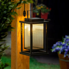Black solar LED lantern in use outdoors, warm light glowing through glass.