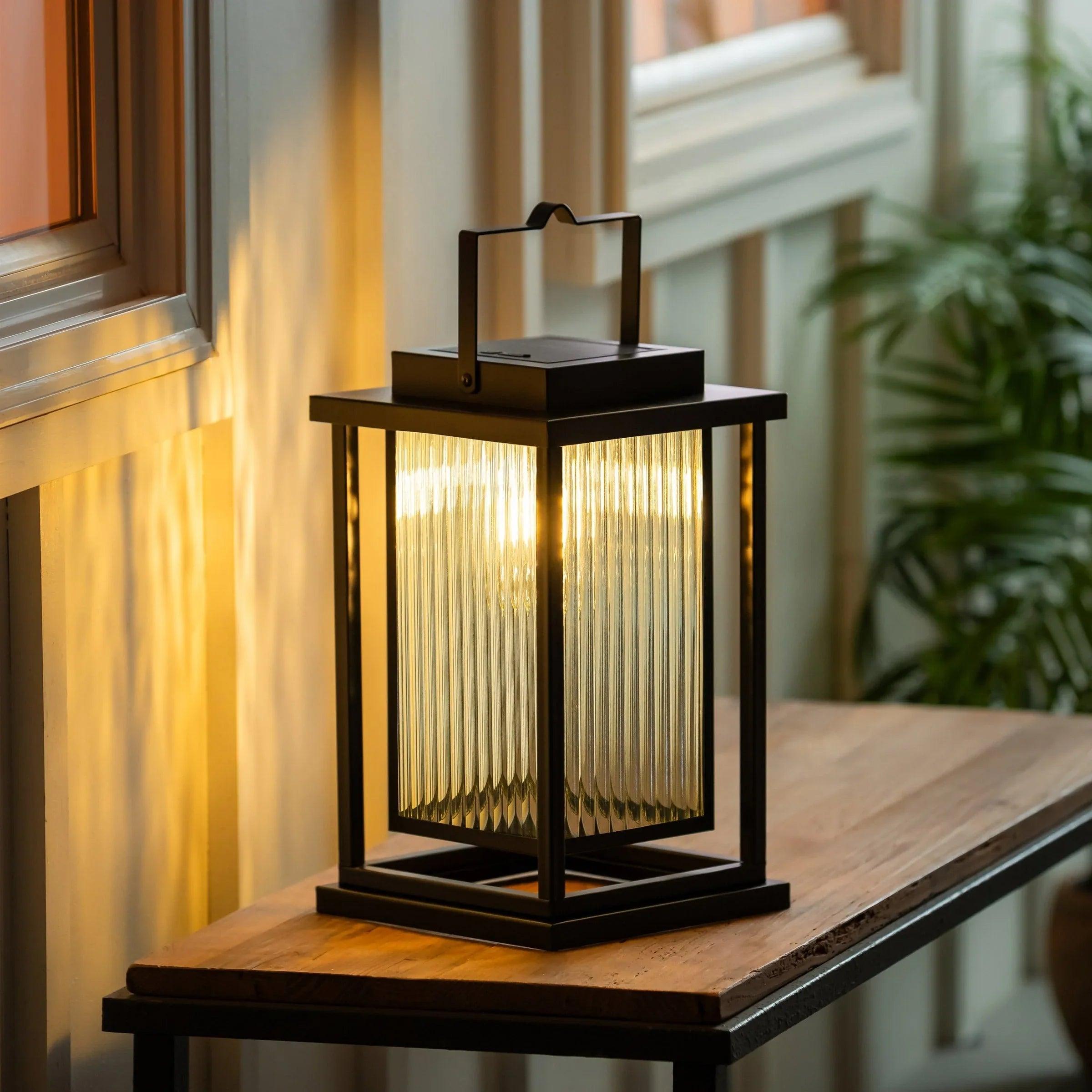 Black solar LED lantern glowing on wooden ledge, warm light through front.