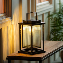 Black solar LED lantern glowing on wooden ledge, warm light through front.