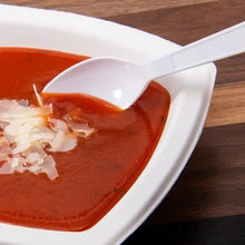 White heavyweight plastic spoon holding red soup in shallow dish