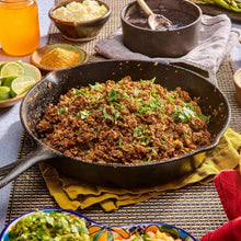 Cast-iron skillet with seasoned taco meat and chopped herbs