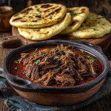 Birria-style shredded beef stew in a dark bowl with chopped cilantro and tortillas