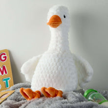 White goose plush with orange beak and feet, sitting on a soft surface.
