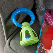 Lime green and blue bell rattle toy resting on a soft surface, handle ring