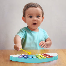 Child playing with rainbow xylophone on wooden table, holding yellow mallet