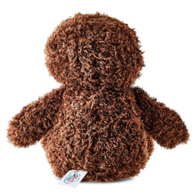 Brown sloth plush toy side/back view with curly fur texture, white face patch, small tag