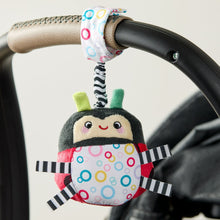 Ladybug plush travel chime clipped to stroller handle, ring patterned body and striped arms