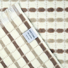 Bath towel edge with fringed trim and attached paper label on a tan dotted design