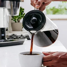 Dark coffee being poured into a cup from a glass carafe
