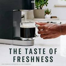 Hand holding a mug while brewing dark coffee in a Keurig-style machine