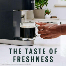 Hand holding a mug of dark coffee from a K-cup coffee maker